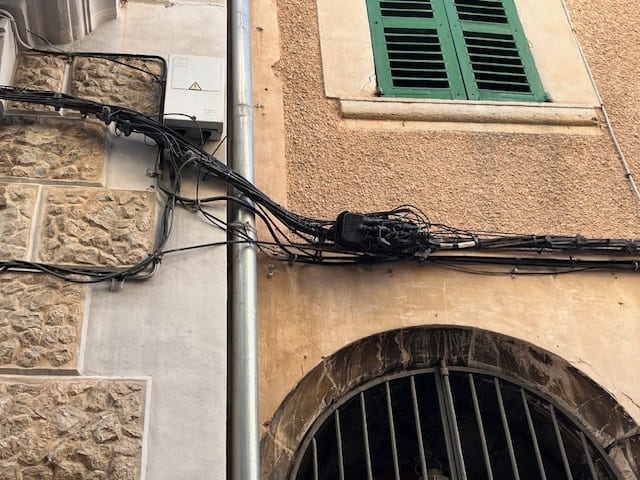 Kabelbündel und Verteiler an einer Fassade mit Fensterladen