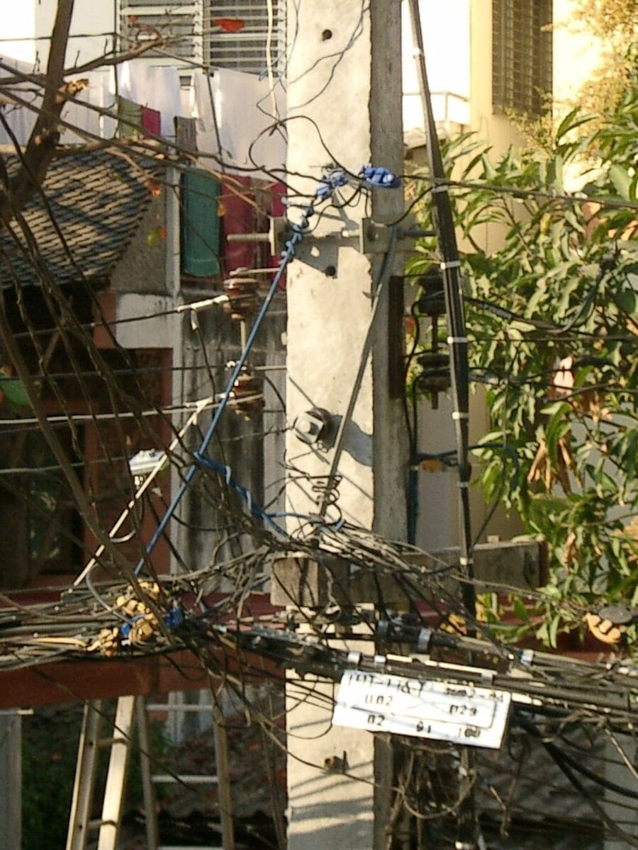 Verzweigte Kabelverbindungen an Betonmast vor einem Wohnhaus